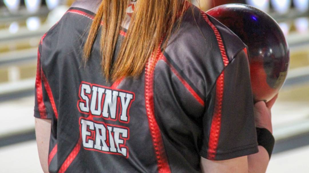 The back of a woman wearing a SUNY Erie Bowling Shirt, holding a bowling ball